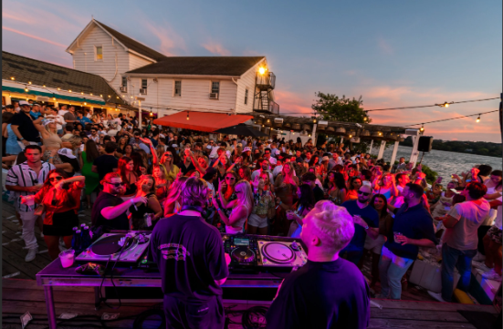 Surf Lodge Montauk waterfront deck during golden hour with guests dining and Fort Pond sunset